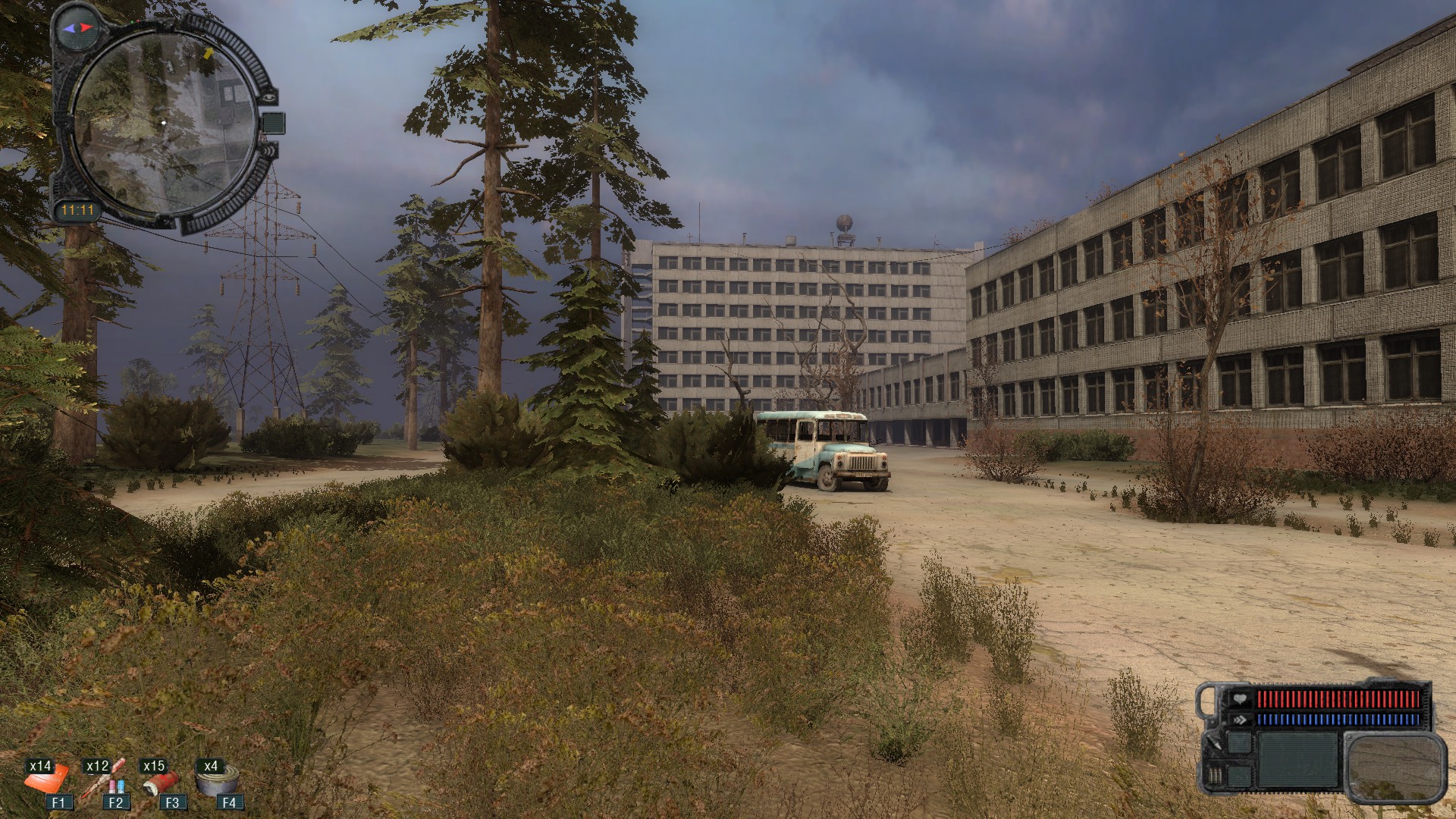 A road leads by an abandoned office building with an old bus in the middle. There's some brush past the road with some evergreens. Military-looking UI is in the corners.