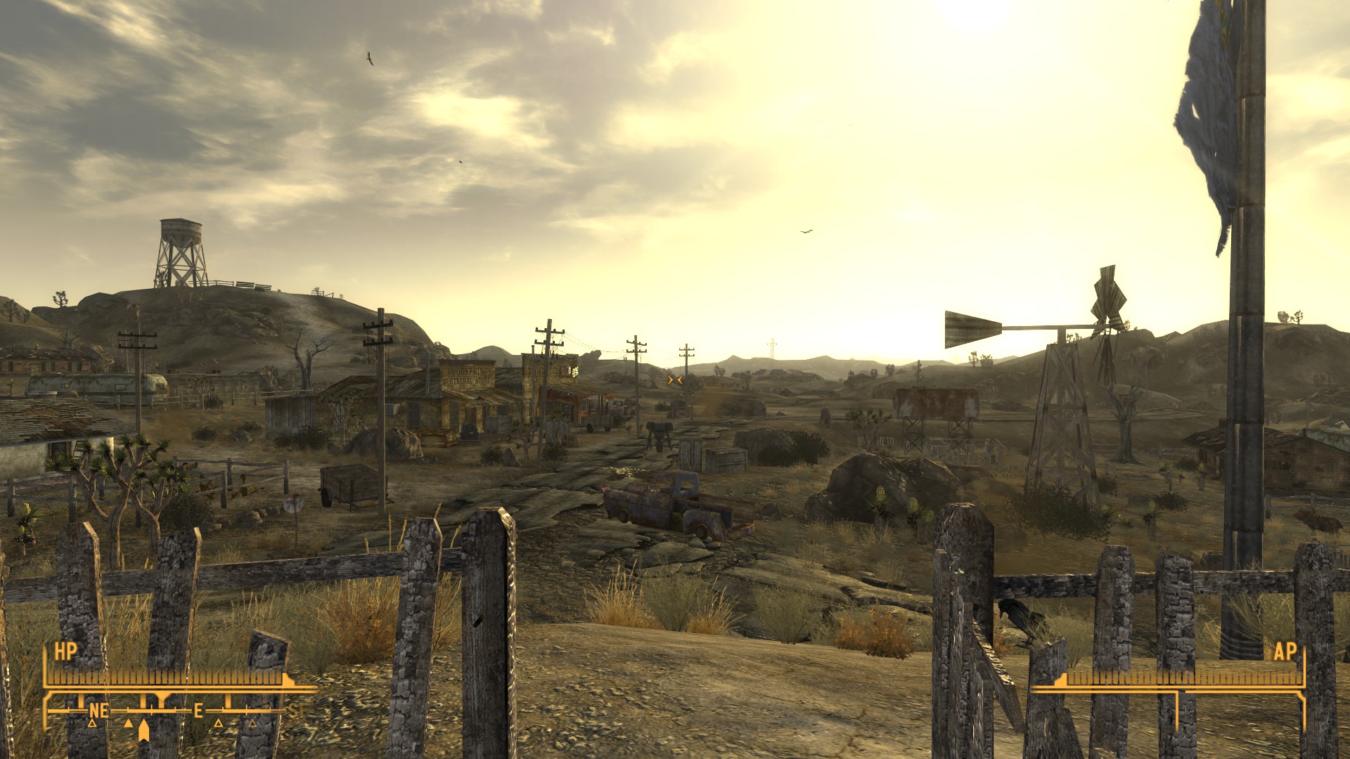 Goodsprings, a small, dusty farming village, is framed by a decaying wooden picket fence. Power lines march along the road that leads toward New Vegas as the sun rises in the east.